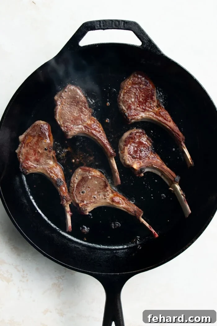 Seared lamb chops lying flat in a cast iron skillet, developing a brown crust.