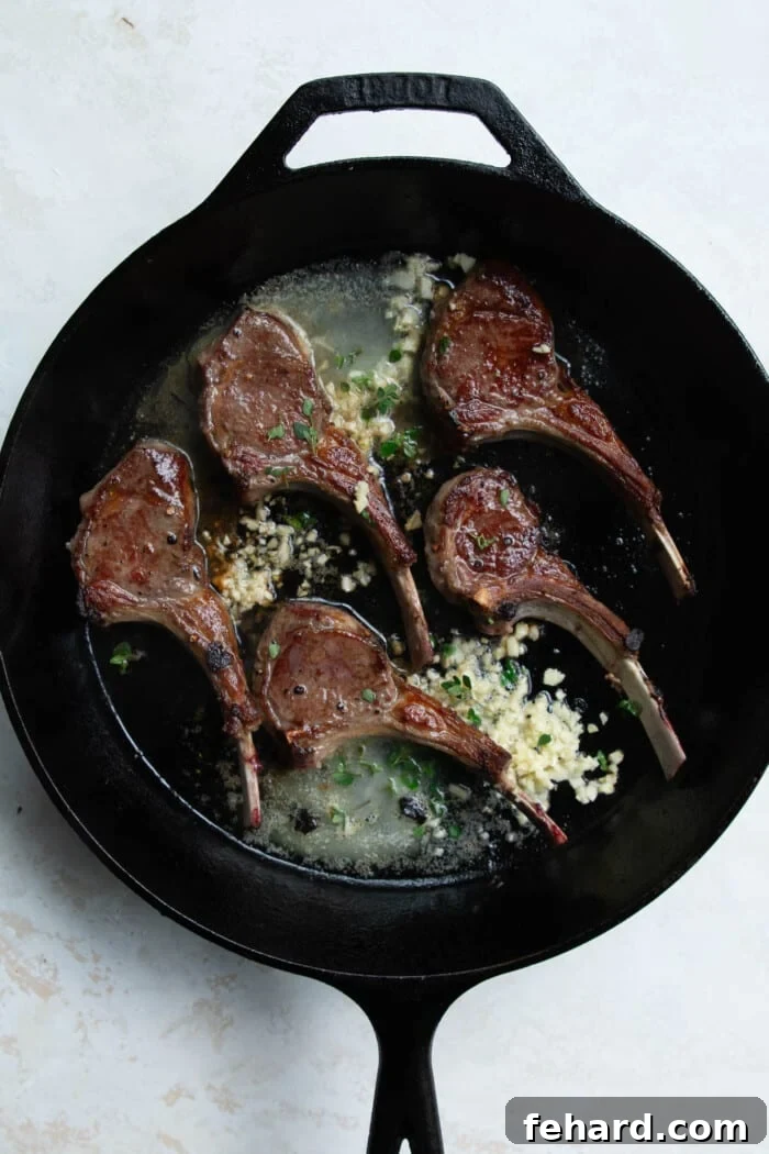 Lamb chops in a skillet being basted with melted butter, garlic, and fresh thyme.