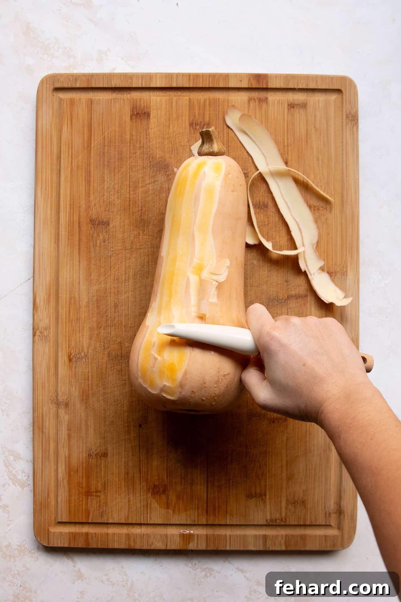 someone peeling a butternut squash on a wooden board. 