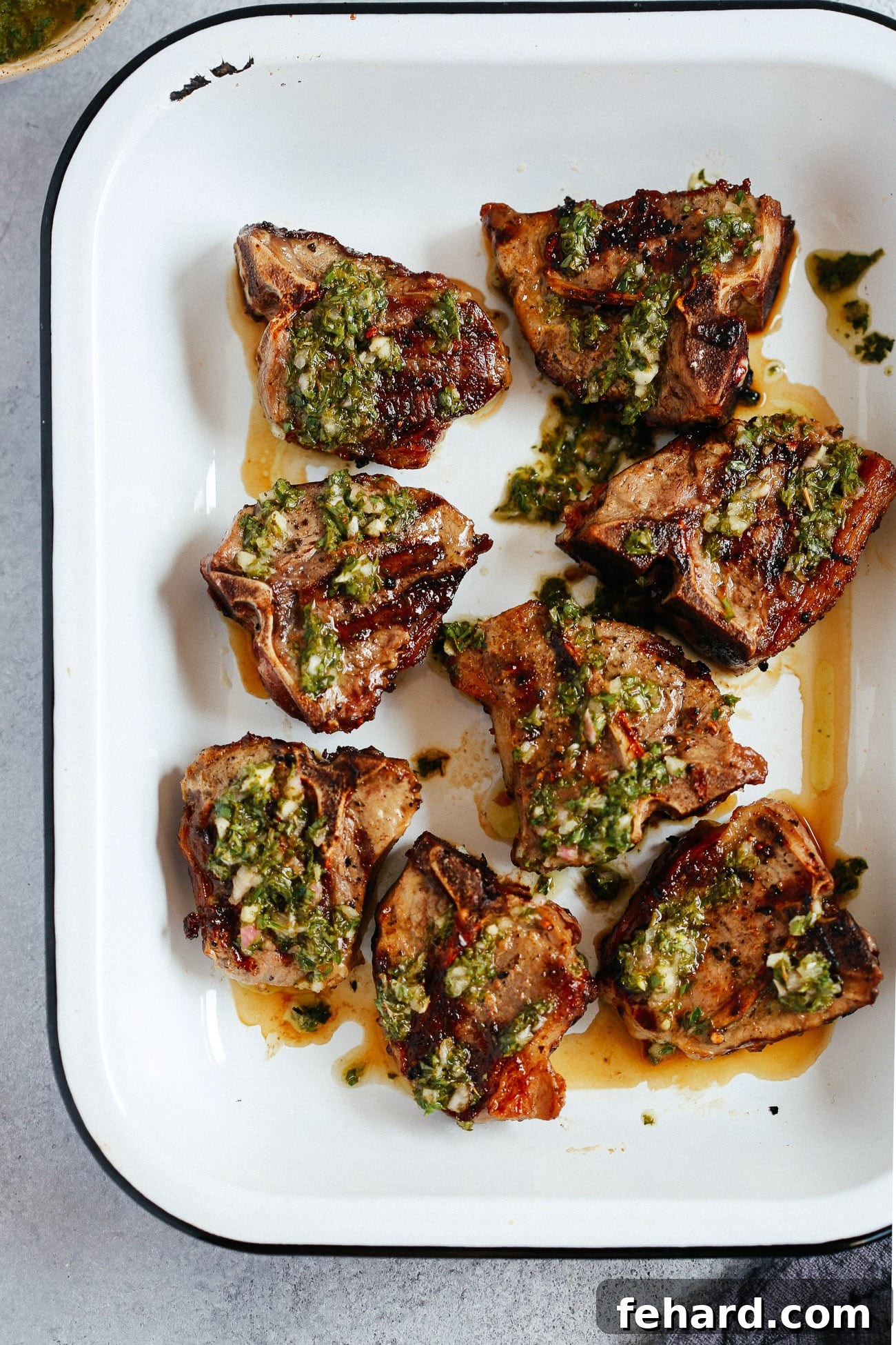 Perfectly grilled lamb chops topped with fresh, vibrant chimichurri sauce, ready to serve on a platter.