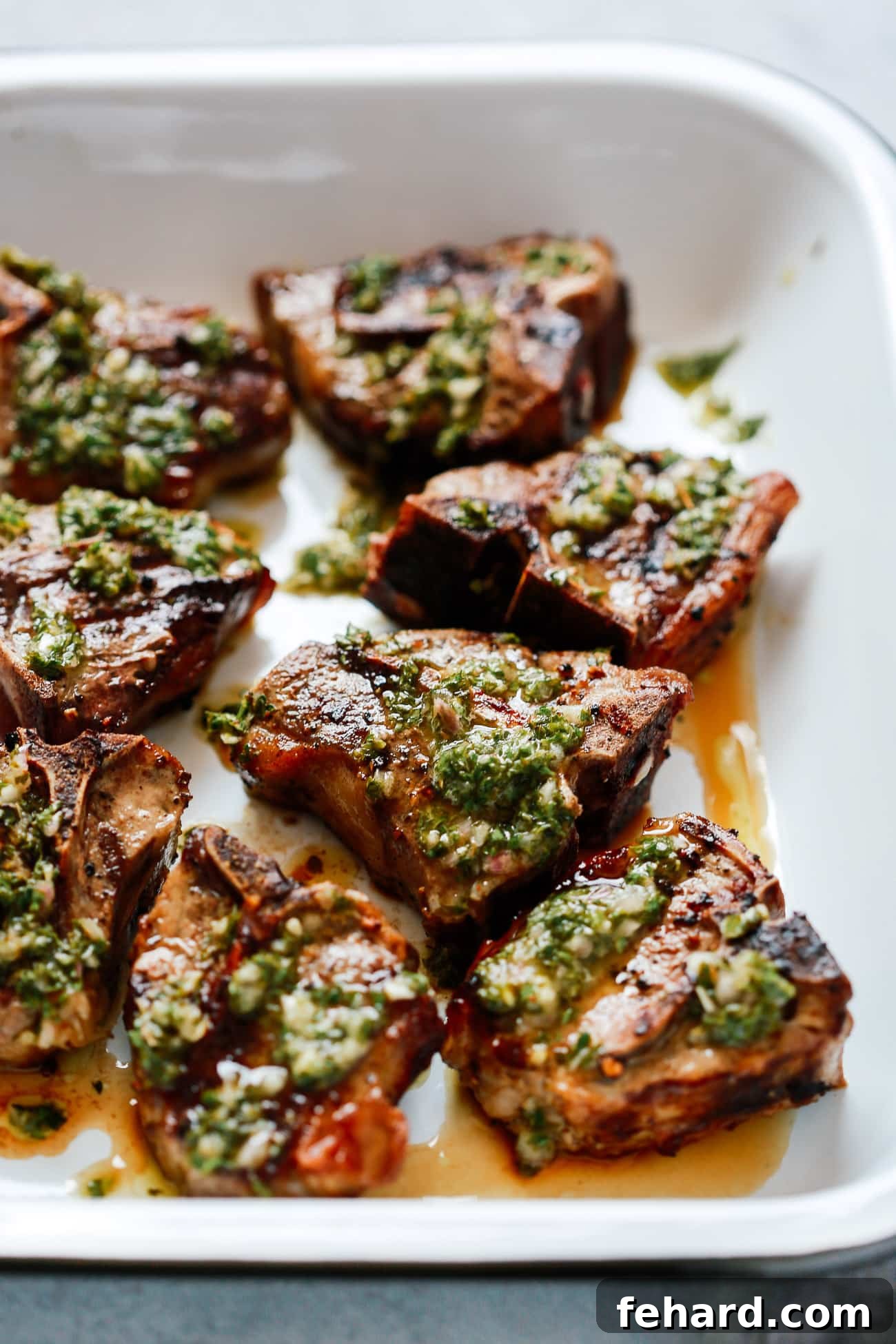 Close-up of lamb shoulder chops coated with vibrant green chimichurri marinade before grilling.