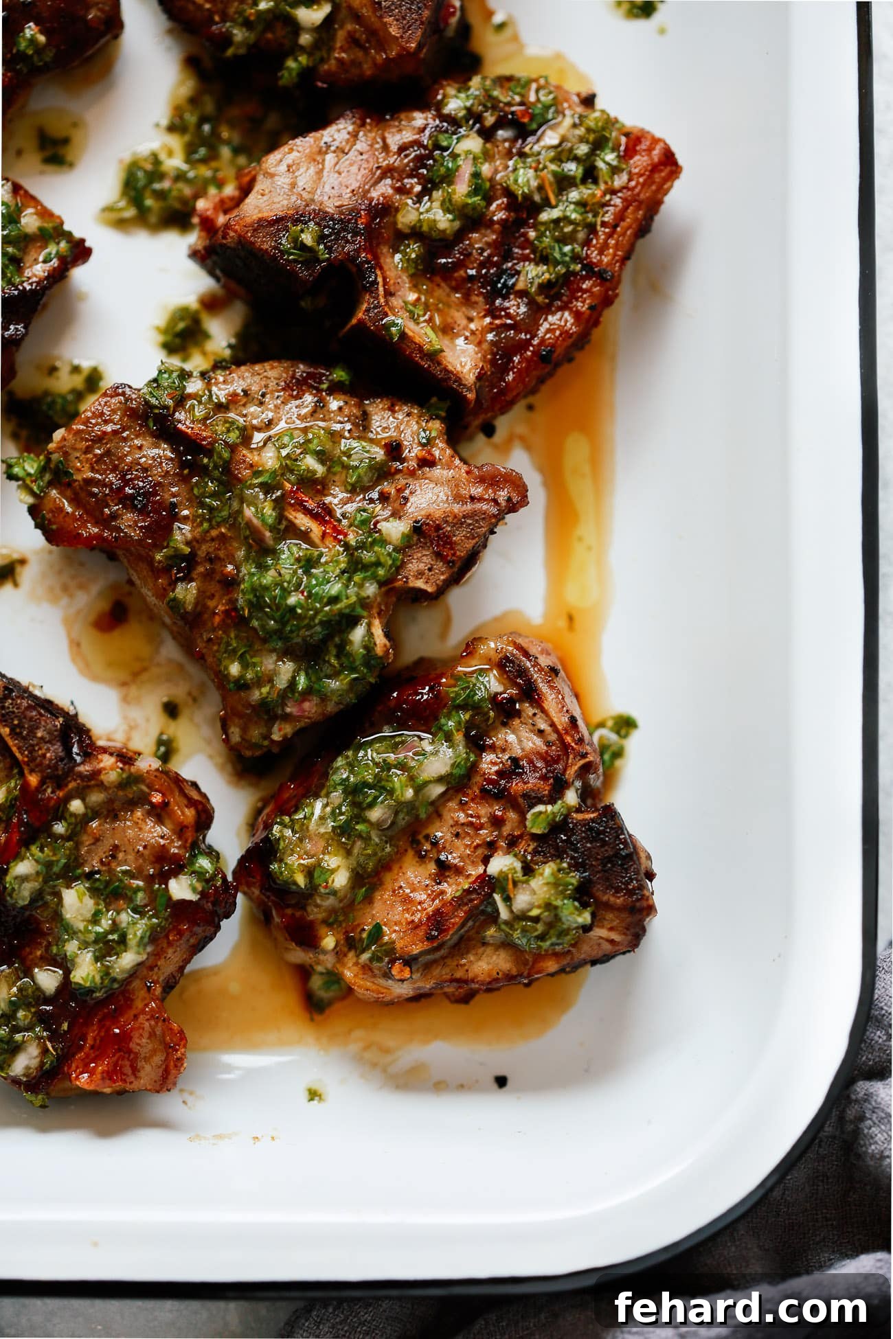 Raw lamb chops in a resealable bag, thoroughly coated in a vibrant green chimichurri marinade, ready for grilling.