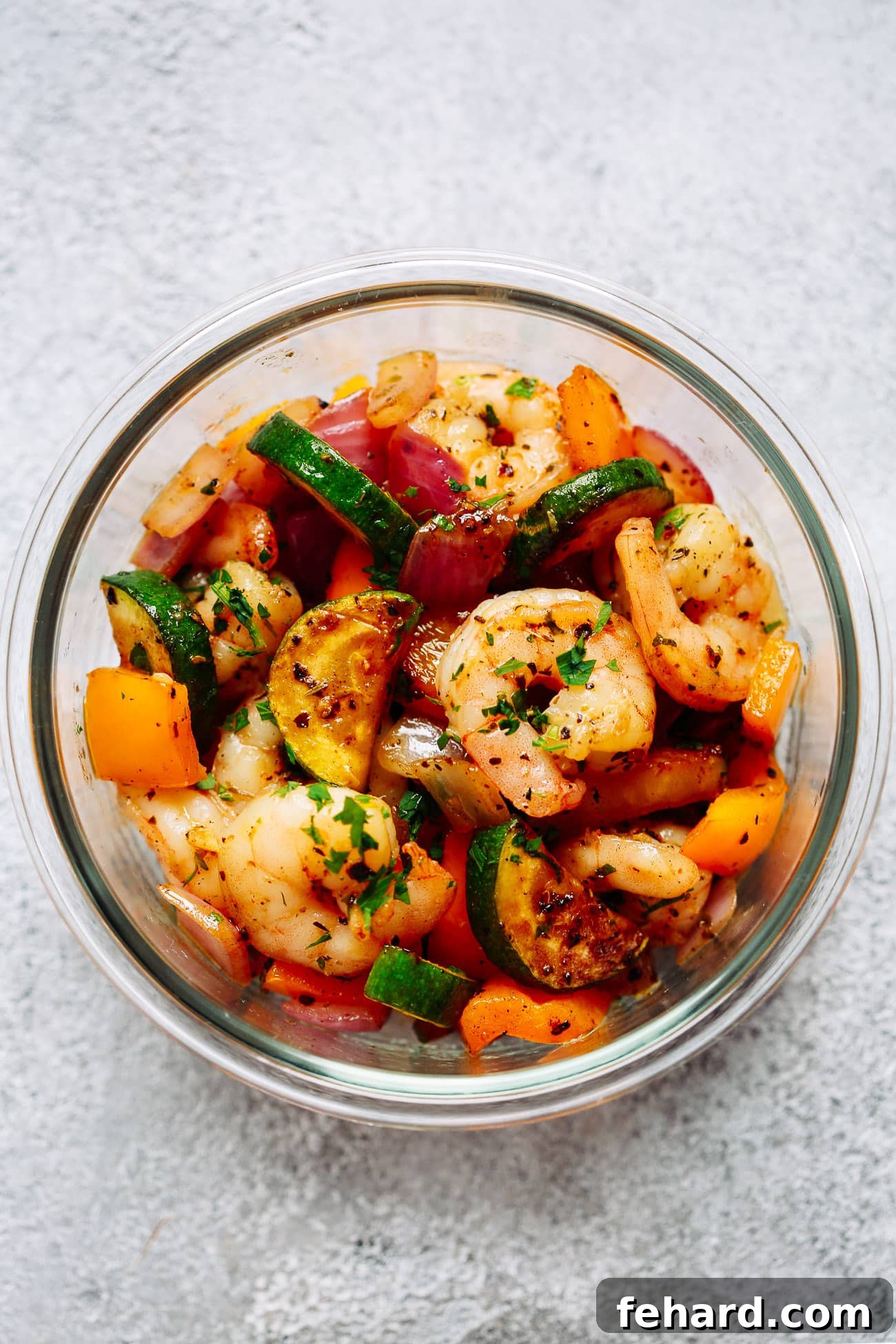 Garlic shrimp and veggies meal prep bowls - a make ahead freezer meal that will save you so much time in the kitchen! Succulent shrimp in garlic butter sauce with zucchini, bell peppers, and onion. This shrimp dinner will become your favorite easy meal prep recipe. close up of a glass bowl containing lots of vegetables and cooked shrimp