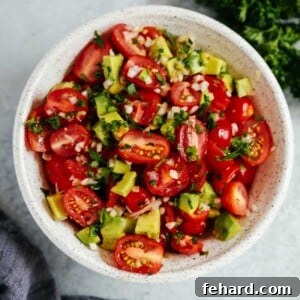 An overhead photo of an avocado tomato salad in a white bowl.