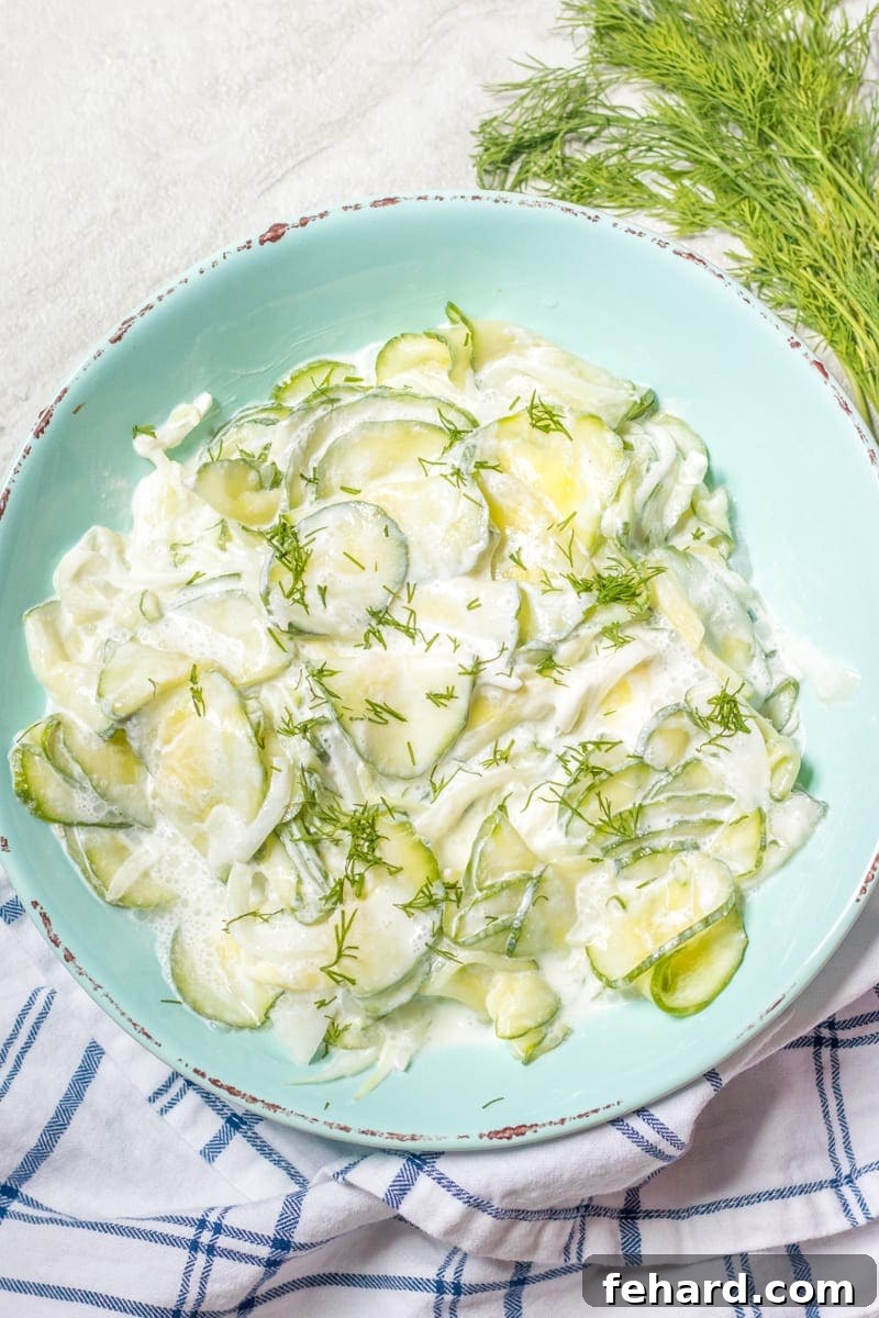 A vibrant bowl of creamy sour cream cucumber salad, generously garnished with fresh dill, presented in an elegant blue serving dish. Perfect for a summer gathering.