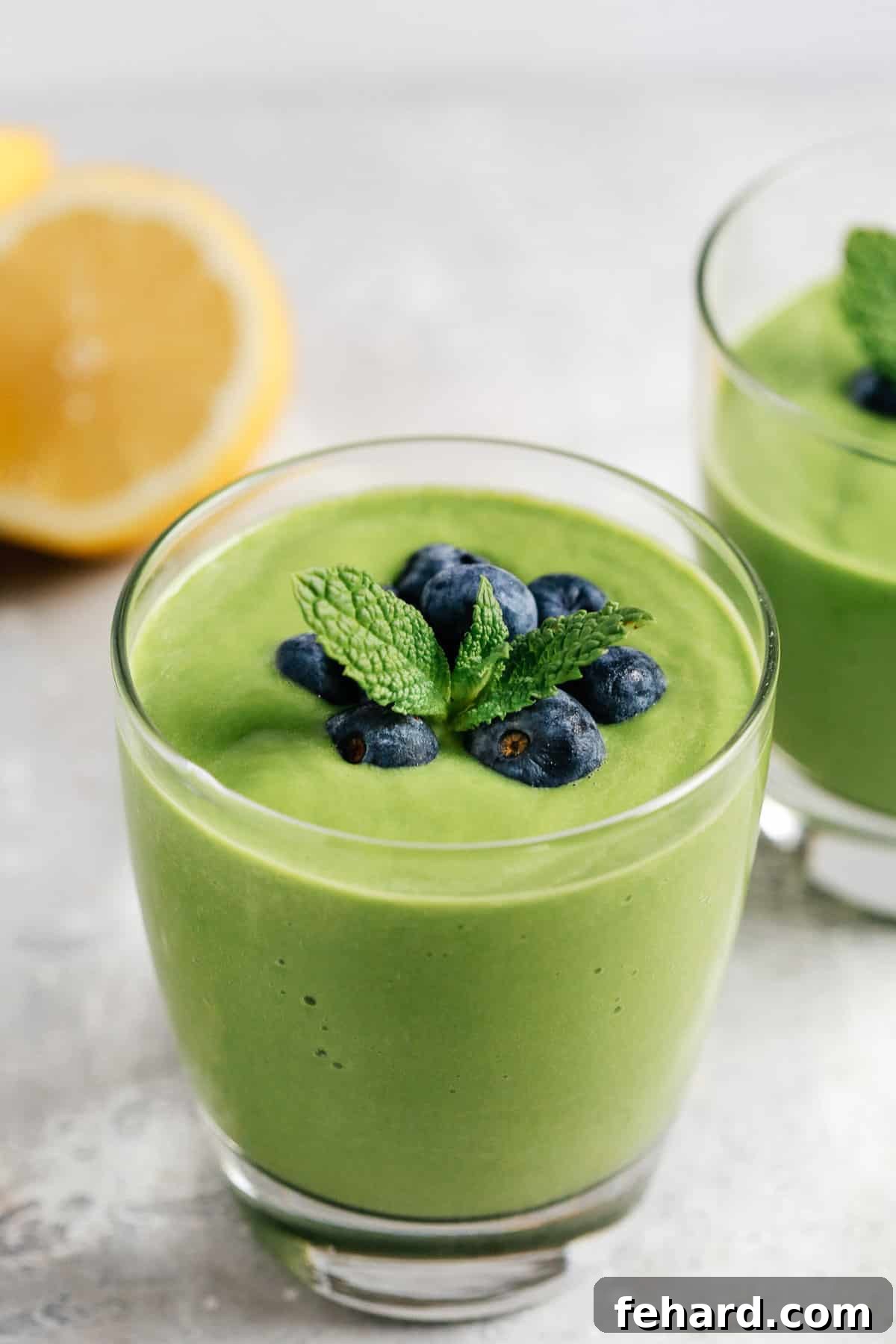 Close up of a glass full of a vibrant green keto smoothie, garnished with fresh mint and blueberries.