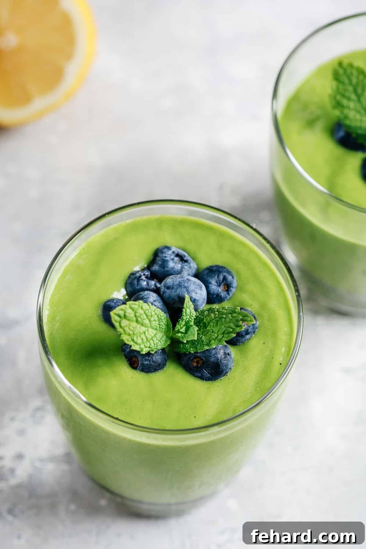 A vibrant green protein shake, beautifully topped with fresh blueberries and a sprig of aromatic mint.