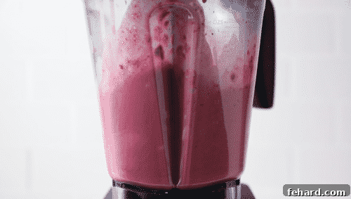 Close-up of a blender actively blending raspberry smoothie ingredients into a smooth, creamy consistency.