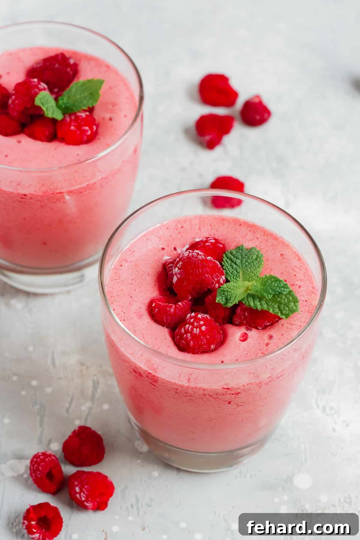 A satisfying and healthy low-carb raspberry smoothie, rich in healthy fats and protein, perfect for a fulfilling breakfast or snack. Two clear drinking glasses filled with a vibrant low-carb raspberry smoothie, garnished with a few fresh raspberries on top.