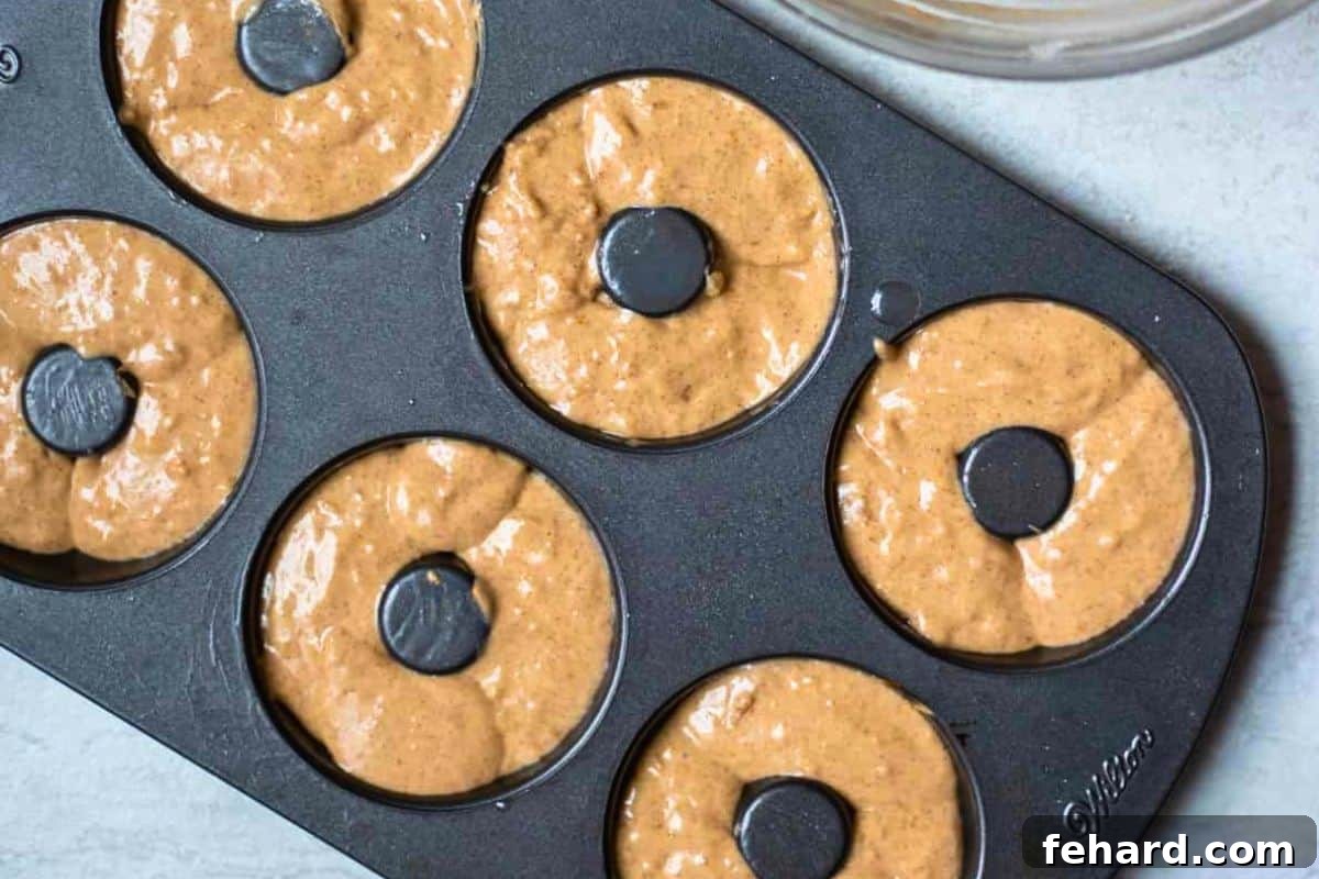 Smooth cinnamon donut batter neatly portioned into each cavity of a donut pan, showcasing even distribution.