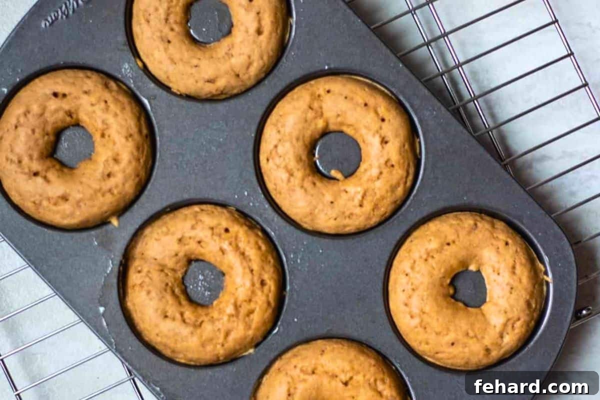 Freshly baked donuts resting in their donut pan on a wire cooling rack, emitting a warm, inviting glow.
