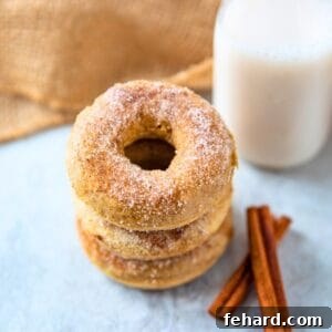 3 baked donuts coated in cinnamon sugar stacked up next to cinnamon sticks and a glass of milk.