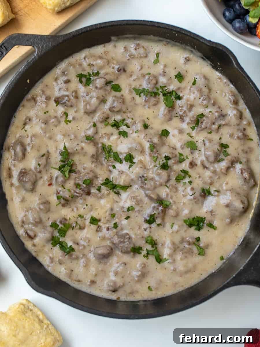 Rich Country Sausage Gravy 2 Sausage Gravy in a cast iron skillet next to homemade biscuits and fresh fruit, ready for a delicious breakfast.