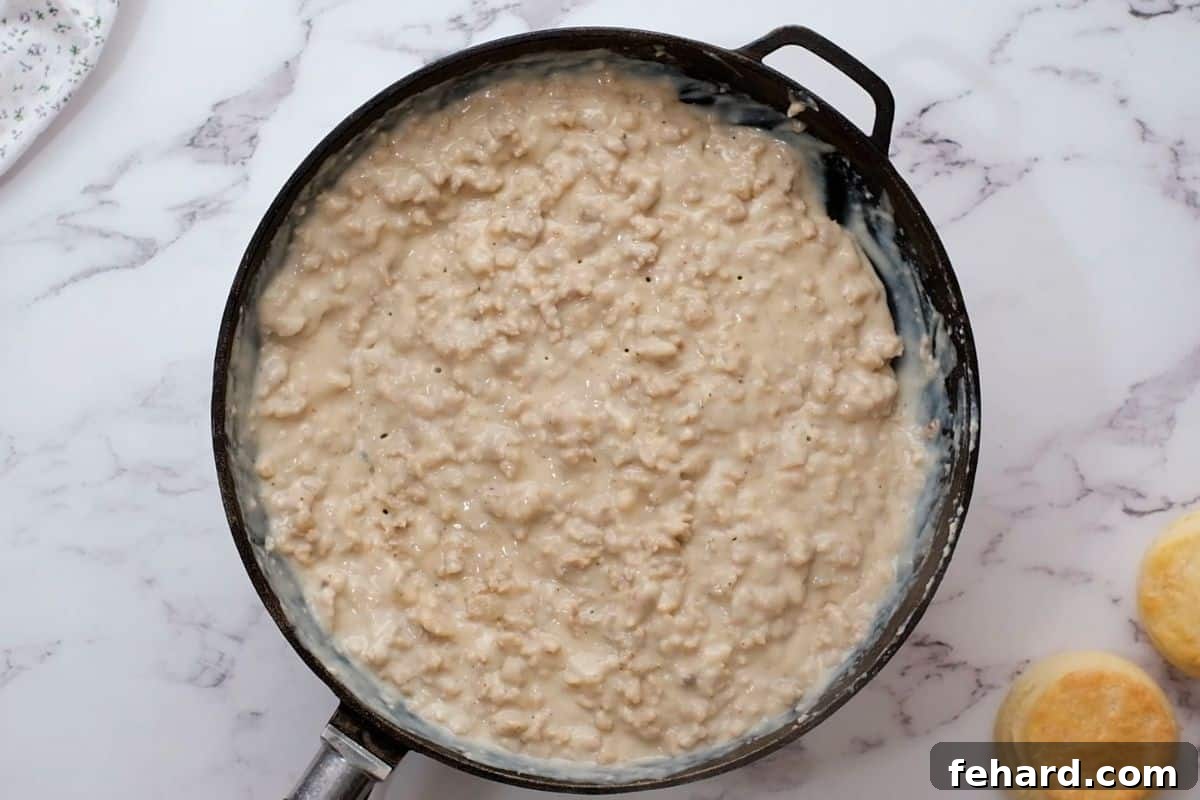 How to make Sausage Gravy Thickened sausage gravy in a skillet, with warm biscuits arranged alongside.