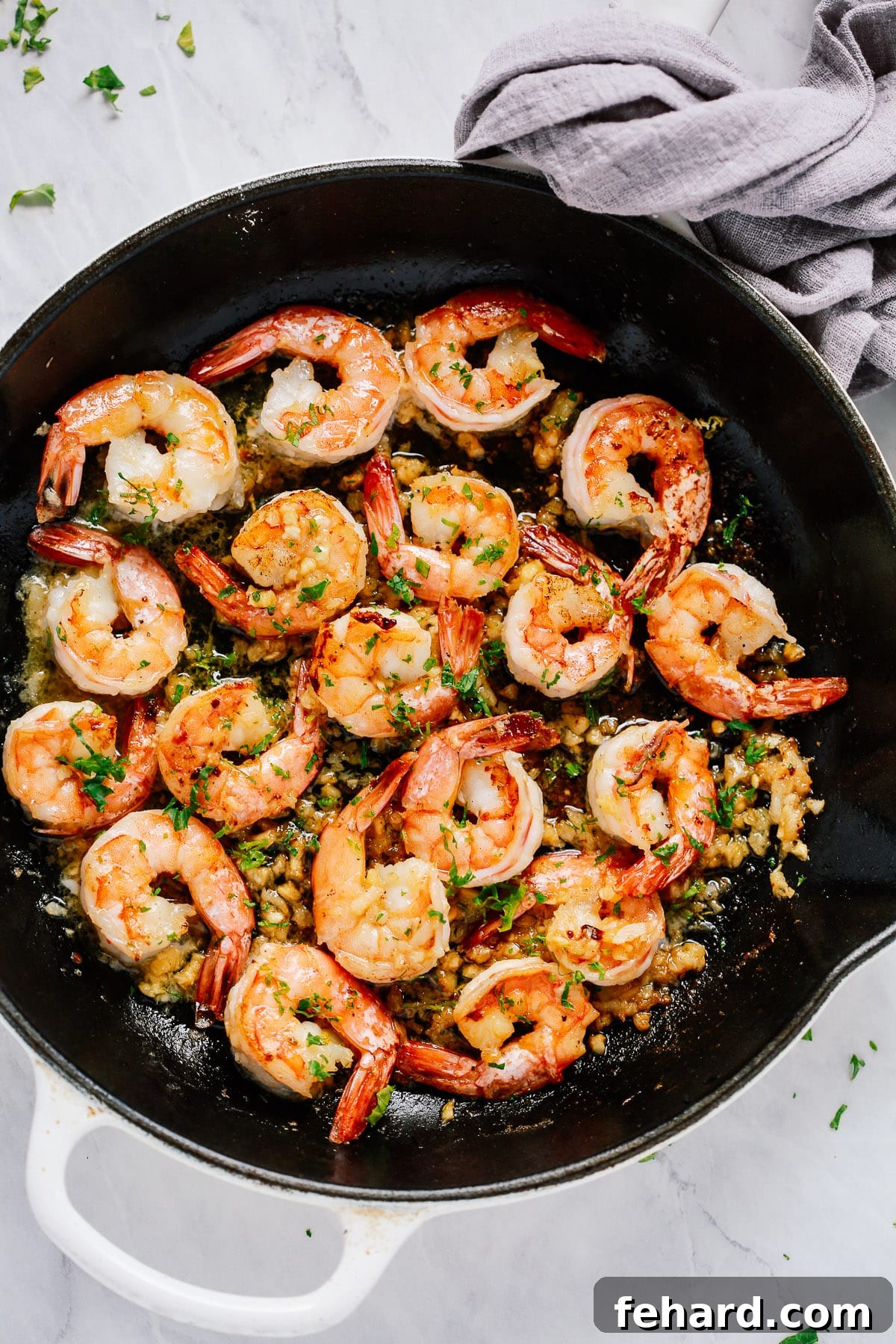 Overhead view of perfectly cooked garlic butter shrimp in a rustic cast iron skillet, garnished with fresh herbs and lemon wedges.