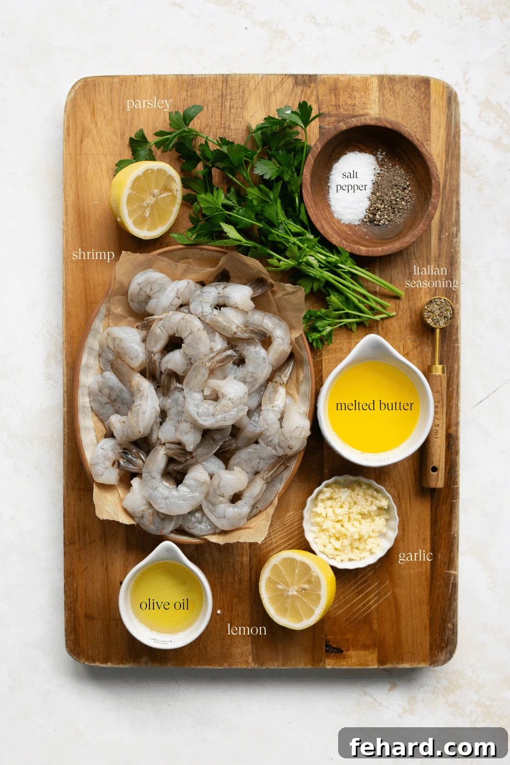 Overhead view of fresh ingredients arranged for making garlic butter shrimp: raw shrimp, garlic cloves, butter, lemon, and olive oil.