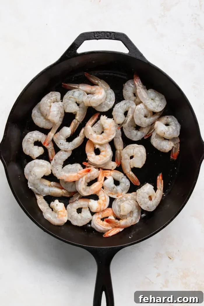 Raw shrimp being added to a hot cast iron skillet with olive oil, ready for searing.