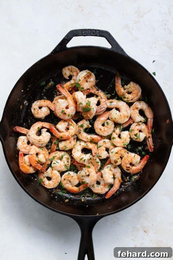 Cooked shrimp being tossed back into the skillet with the garlic butter sauce.