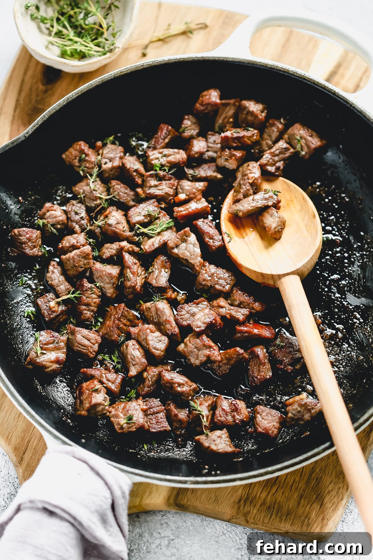 Closeup of sizzling garlic butter steak bites cooking in a black cast iron skillet.