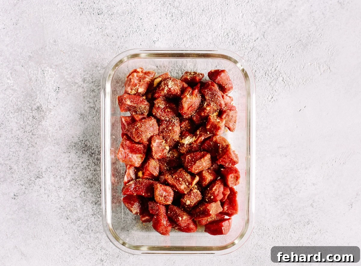 Raw beef sirloin cut into cubes in a glass meal prep container, seasoned and ready for cooking.