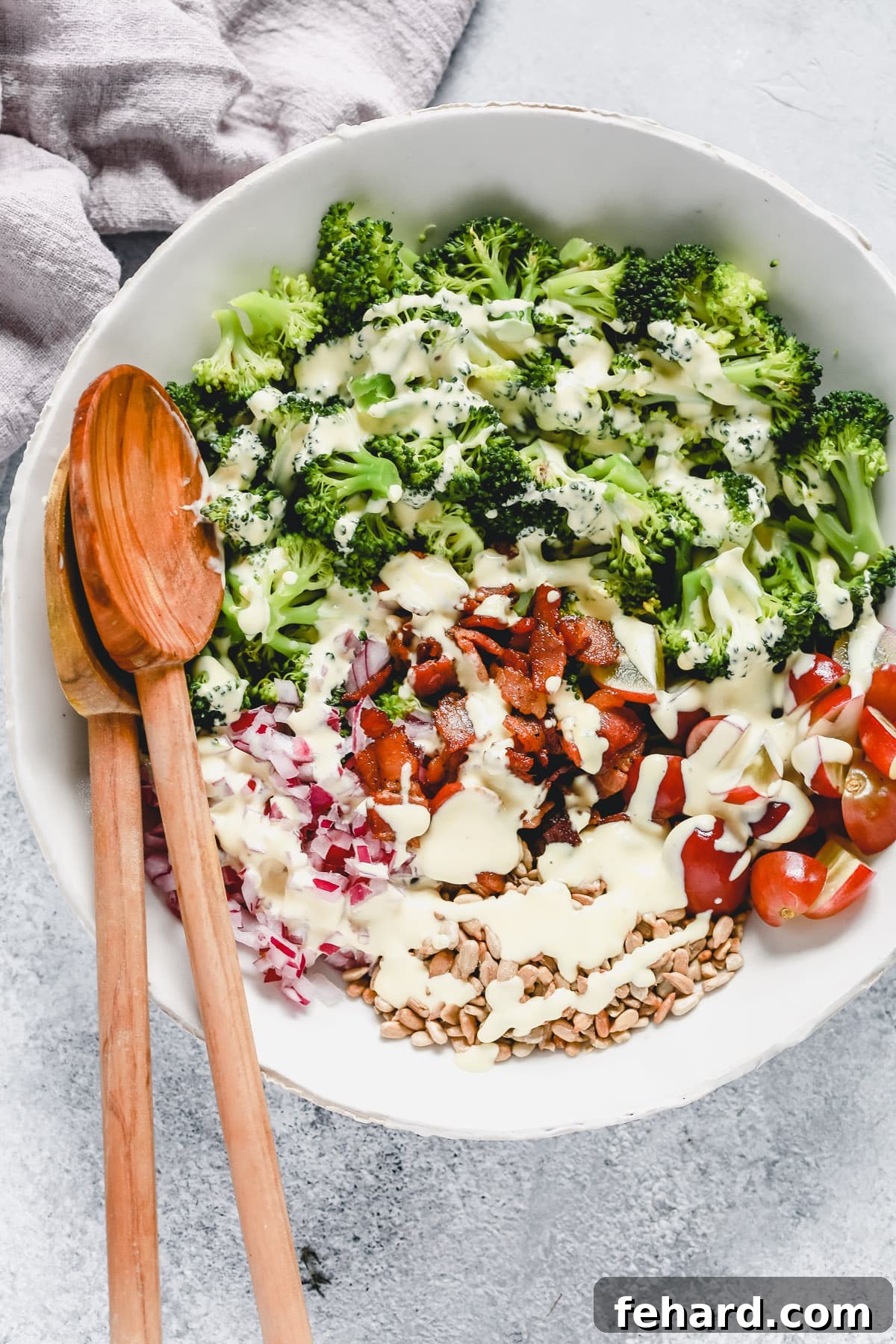 A Closer Look at the Vibrant Ingredients of Our Easy Broccoli Salad Colorful broccoli salad in a white bowl, showcasing broccoli, tomatoes, bacon, onion, and sunflower seeds with dressing