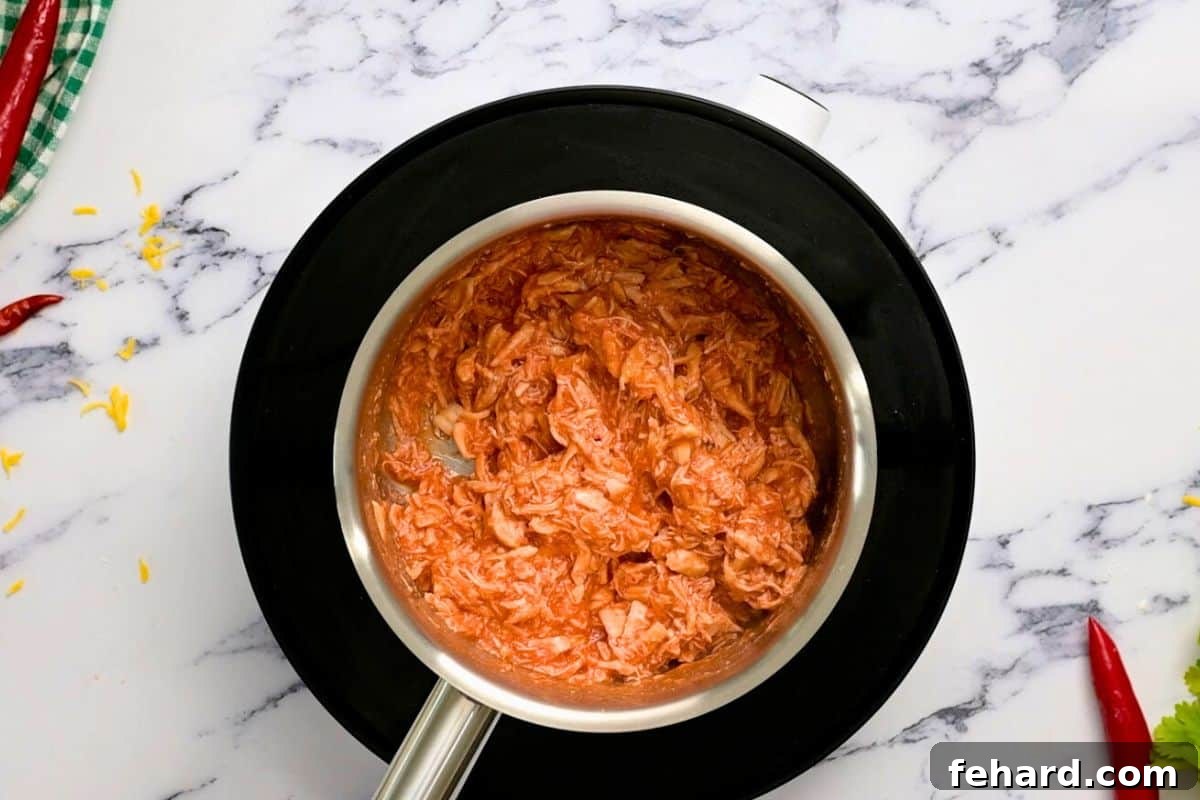 Buffalo Sauce Coated Chicken for Pizza Shredded cooked chicken coated evenly in homemade buffalo sauce, ready to be spread onto the pizza crust.