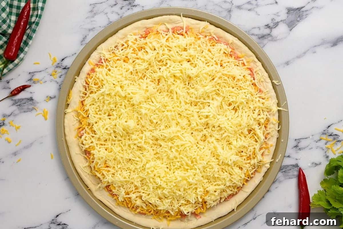 Assembled Buffalo Chicken Pizza An assembled pizza before baking, topped with buffalo chicken and a generous layer of cheddar and mozzarella cheese, ready for the oven.