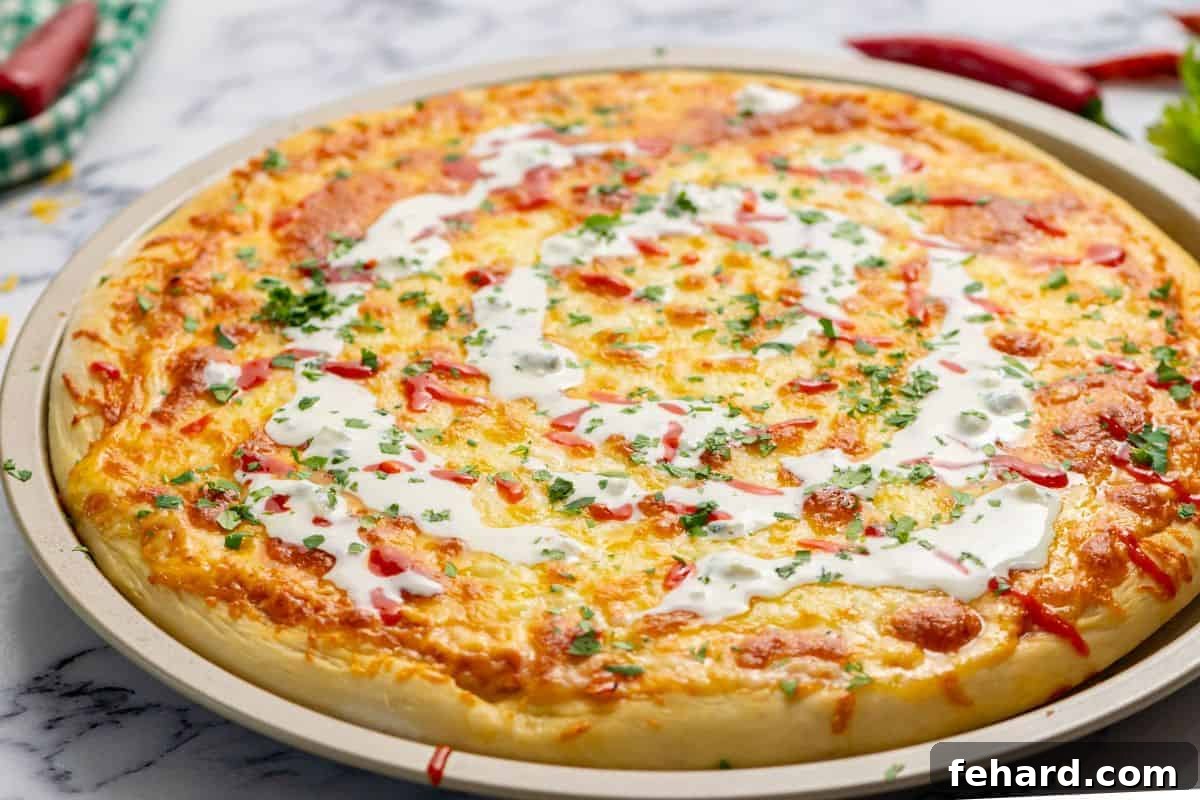 Hot Wing Pizza 3 A freshly baked Buffalo Chicken Pizza, glistening with melted cheese and a decorative swirl of ranch dressing, ready to be sliced and served.