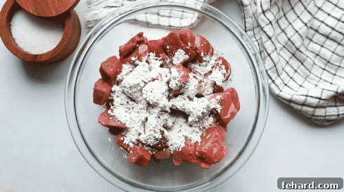 overhead view of a glass bowl containing beef stew meat cover with flour