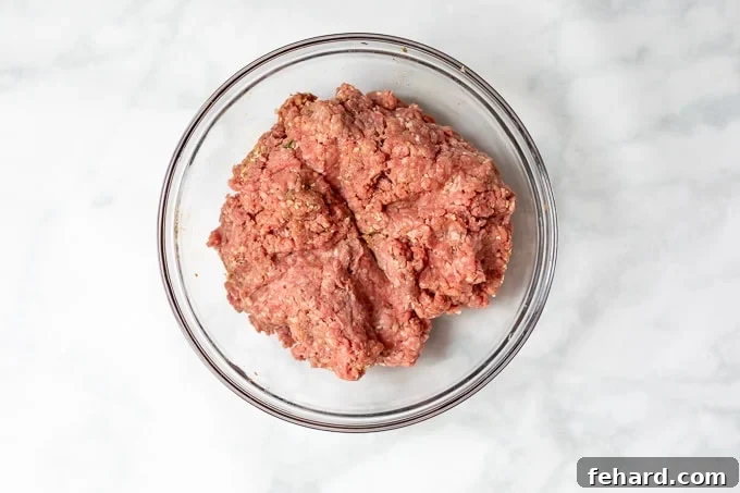 Seasoned ground beef mixture in a glass bowl, gently scored into four equal sections, preparing for patty formation.