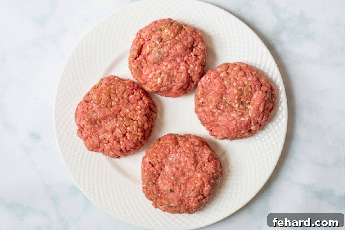 Four perfectly shaped 6-ounce hamburger patties resting on a white plate, intentionally crafted to be slightly larger than standard buns to account for shrinkage.