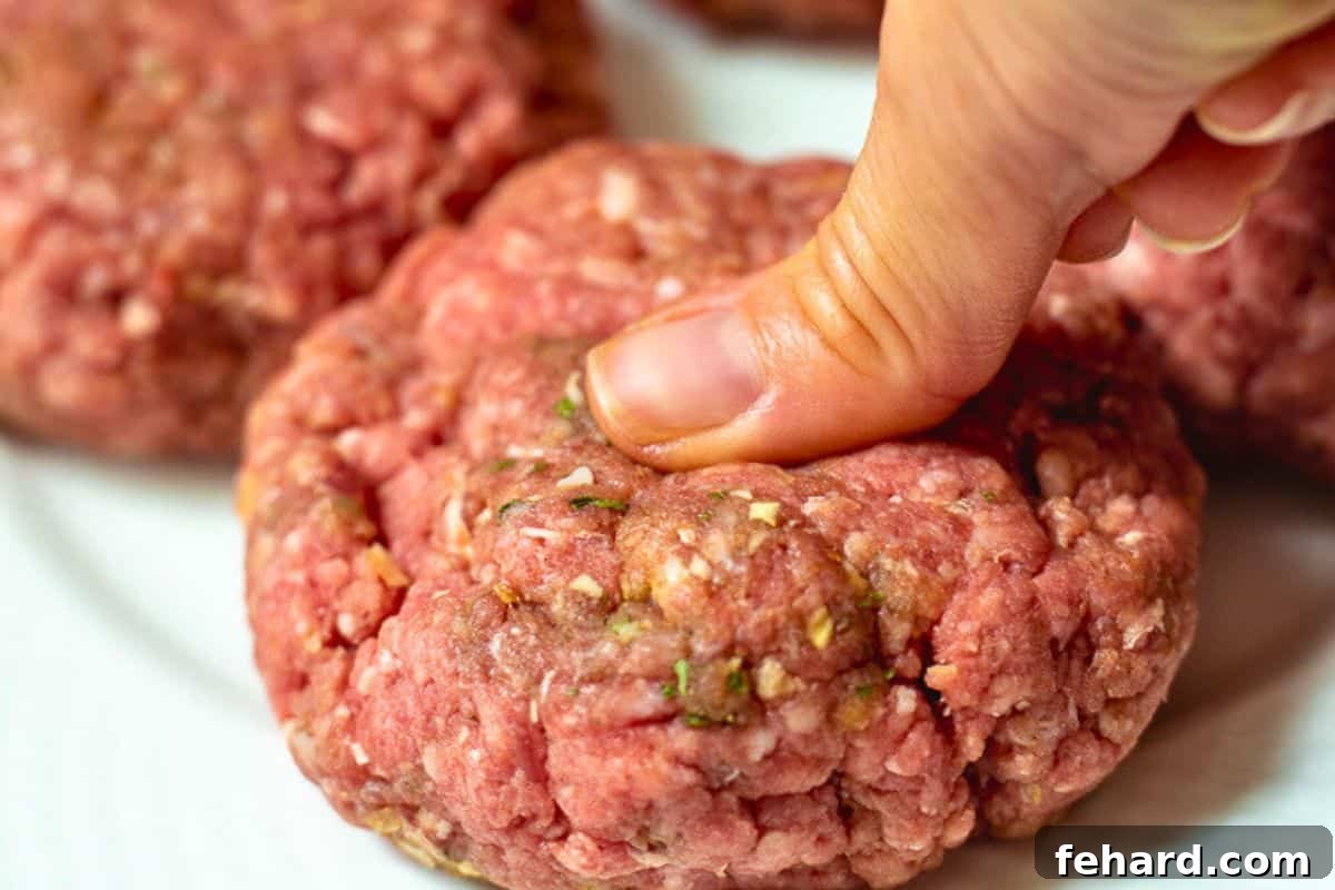 A thumb gently pressing a shallow indentation into the center of a homemade burger patty, a crucial step for even cooking and preventing shrinkage.