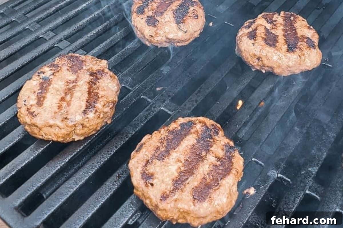 Four perfectly cooking 6-ounce hamburgers on a gas grill, having just been flipped once, showing a delicious char.