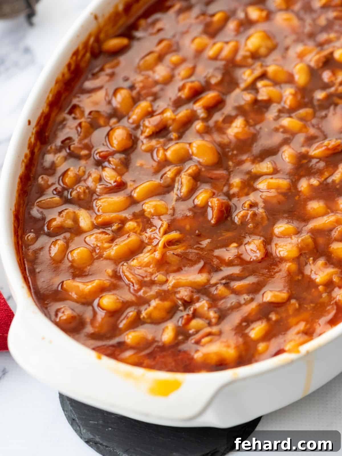 Homemade baked beans in large white casserole dish, garnished with fresh herbs.