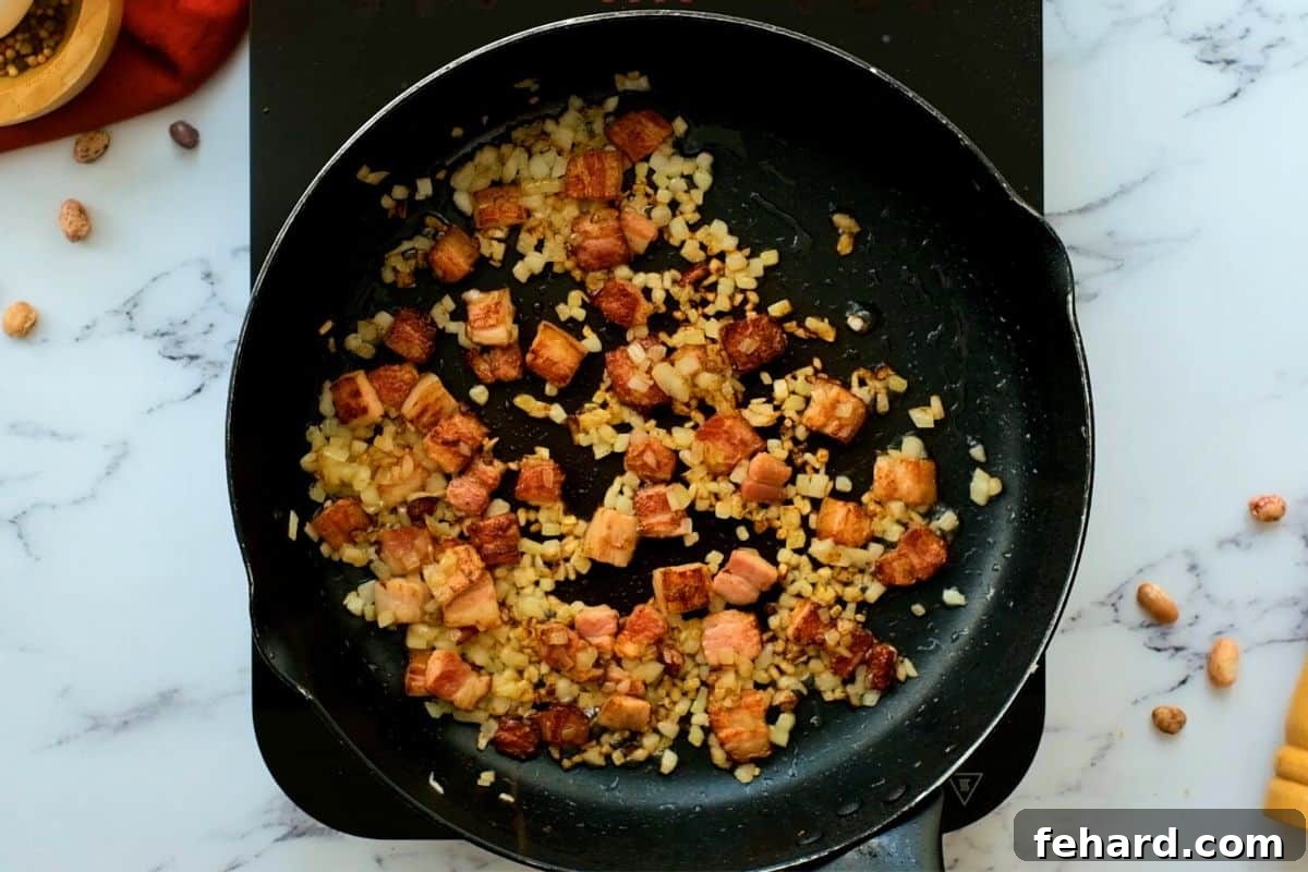 Cubed bacon and minced onion sautéing together in a large pan.