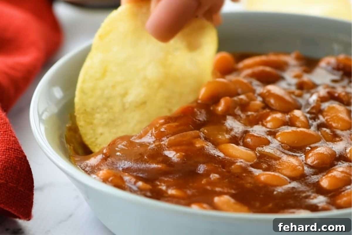 A plain potato chip dipping into rich homemade baked beans.