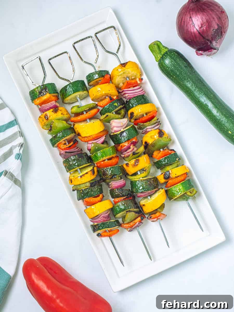 Beautifully grilled vegetable kabobs featuring red bell peppers, summer squash, green peppers, and onions, artfully arranged on a white platter, ready to be served.