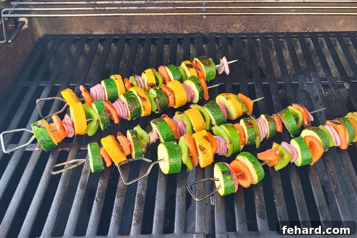 Vibrant veggie kabobs, made with marinated red bell peppers, summer squash, green peppers, and onions, sizzling on a hot grill with visible char marks.