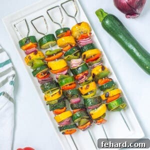 Veggie Kabobs made with marinated red bell peppers, summer squash, green peppers and onions on white platter after being grilled.