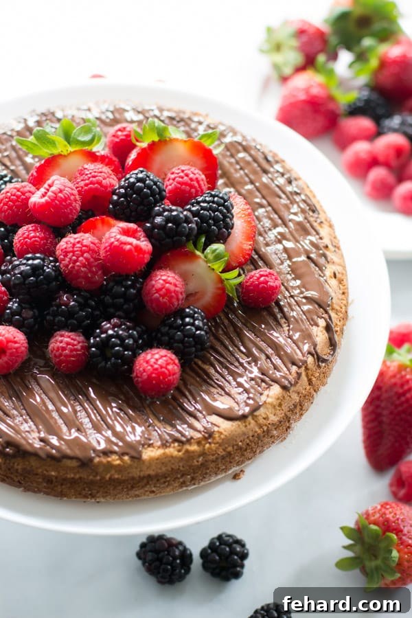 A close-up shot of the finished almond cake, generously topped with an assortment of vibrant fresh berries, highlighting its natural beauty and inviting texture.