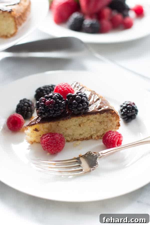 A single slice of the almond cake with berries, served on a white plate alongside a fork, showcasing its soft crumb and fresh fruit topping.