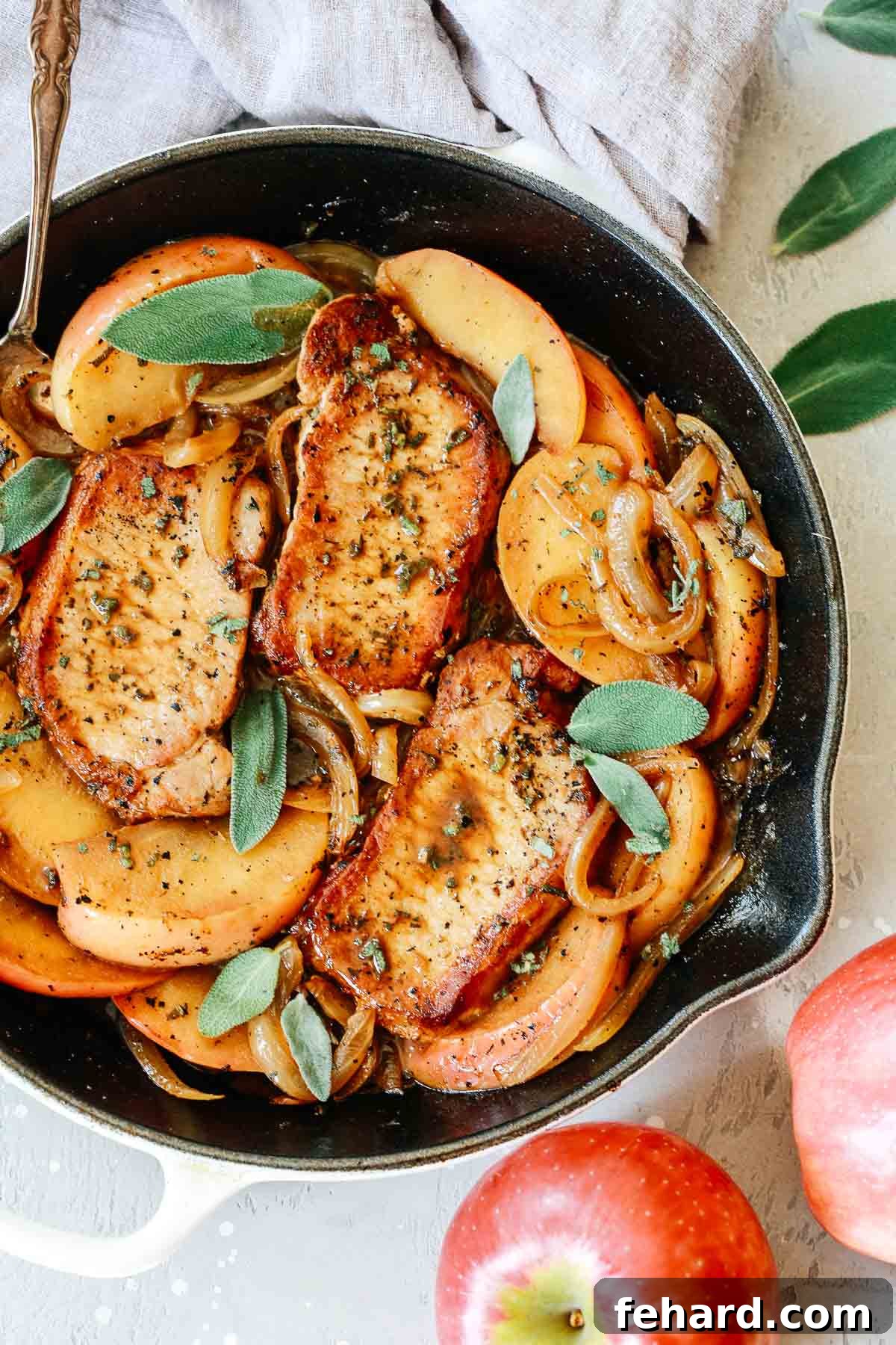 Complete skillet dinner with pork chops, apple slices, and onions, garnished with fresh herbs, ready for serving.