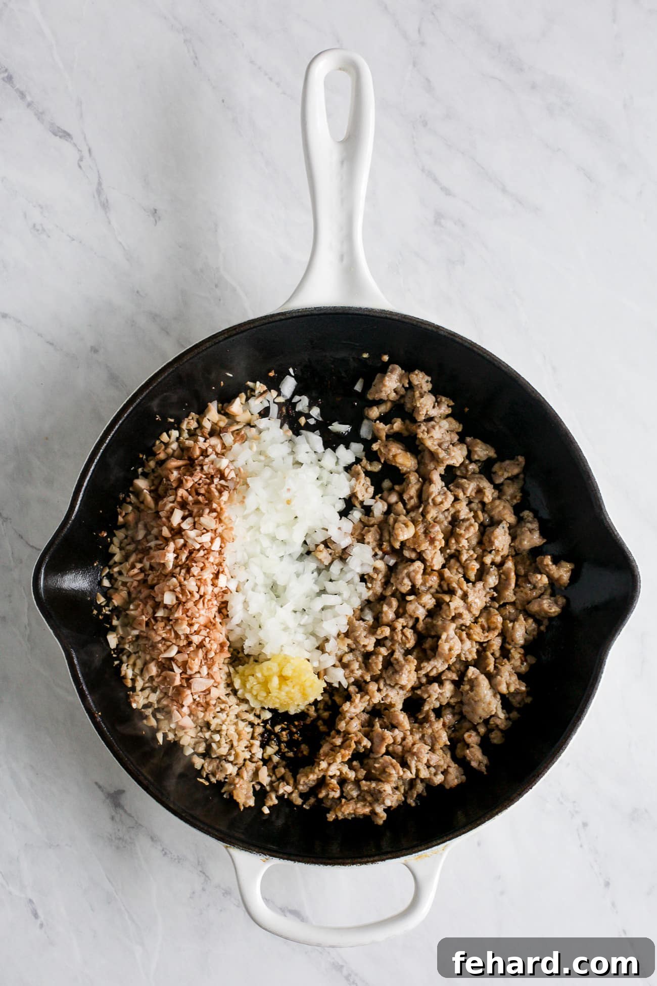 A skillet on the stove containing a savory mixture of browned sausage, diced onion, minced garlic, and chopped mushroom stems.