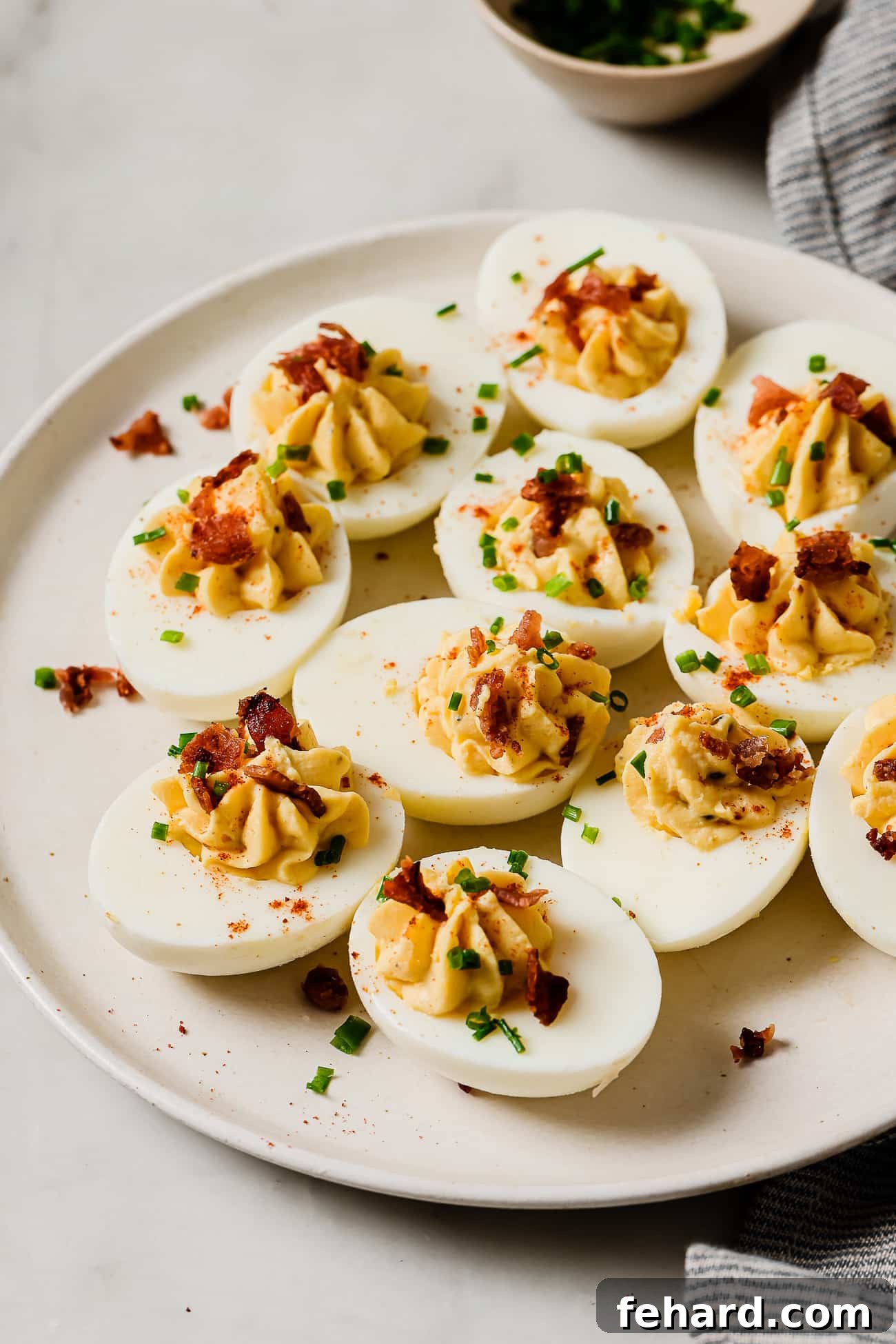 A beautifully arranged platter of easy deviled eggs garnished with fresh chives, crispy bacon bits, and a dusting of vibrant paprika.