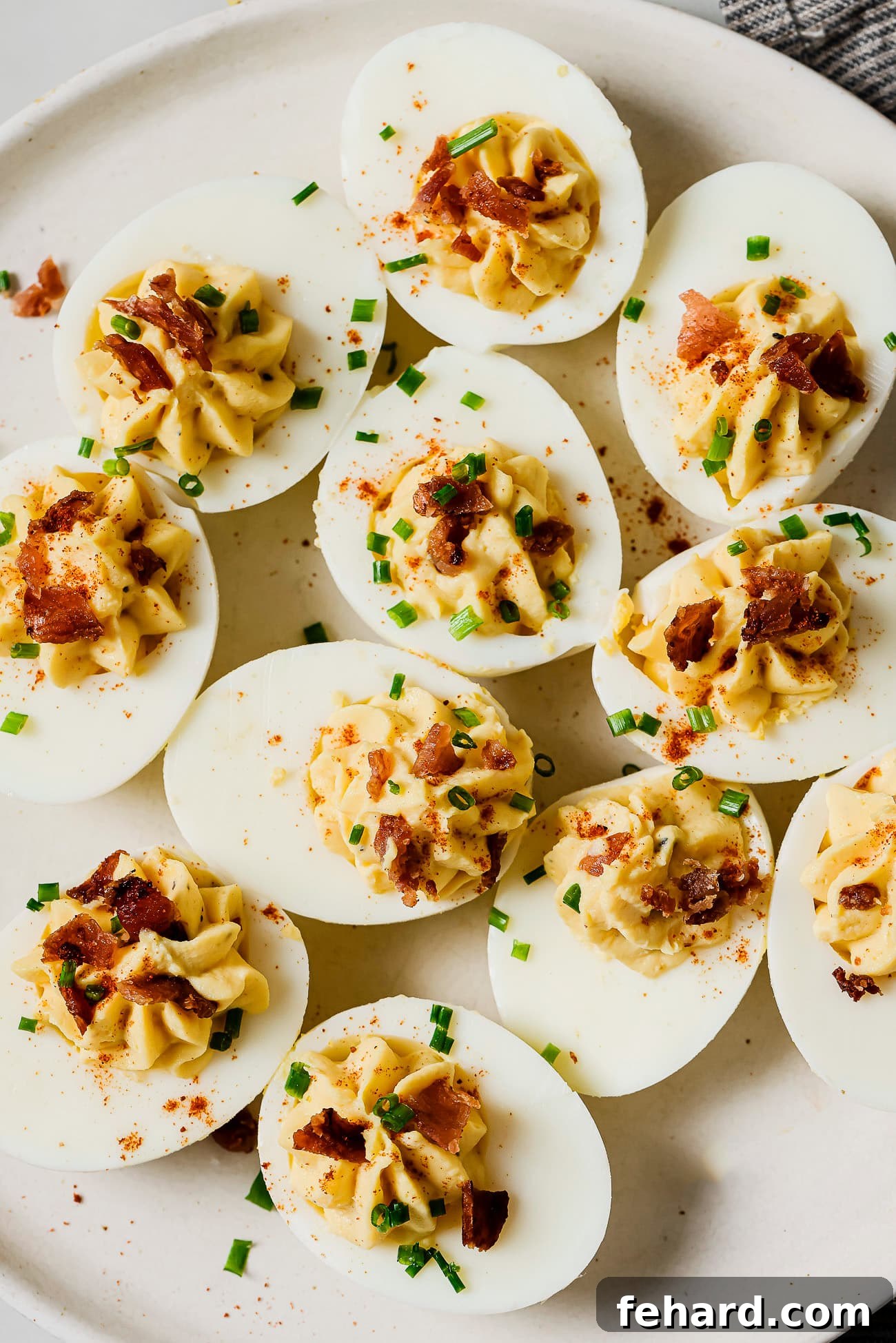 A platter of exquisitely prepared deviled eggs, featuring a creamy filling, dusted with paprika, and adorned with fresh herbs, ready for serving.