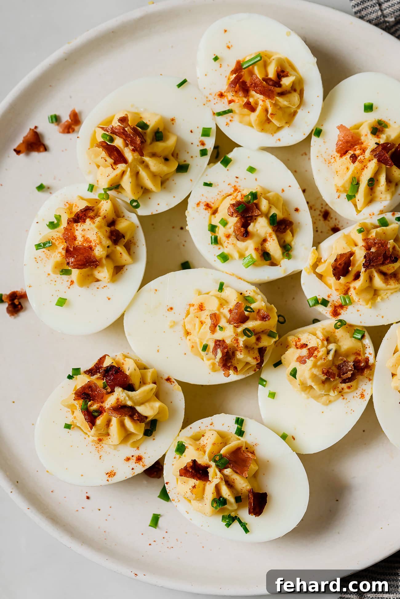 A pristine white platter filled with perfectly presented deviled eggs, garnished with a light dusting of paprika and fresh green herbs, ready to be enjoyed.