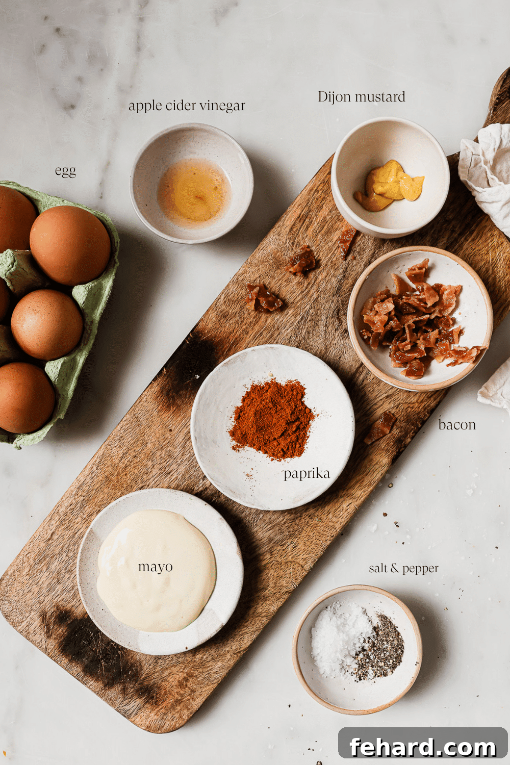 A vibrant collection of ingredients for easy deviled eggs laid out on a elegant marble board, including hard-boiled eggs, mayonnaise, mustards, vinegar, spices, and fresh herbs.