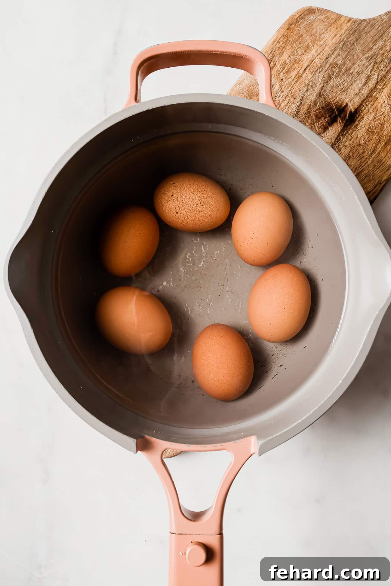 Eggs submerged in a pan of warm water, just beginning to boil on the stove.