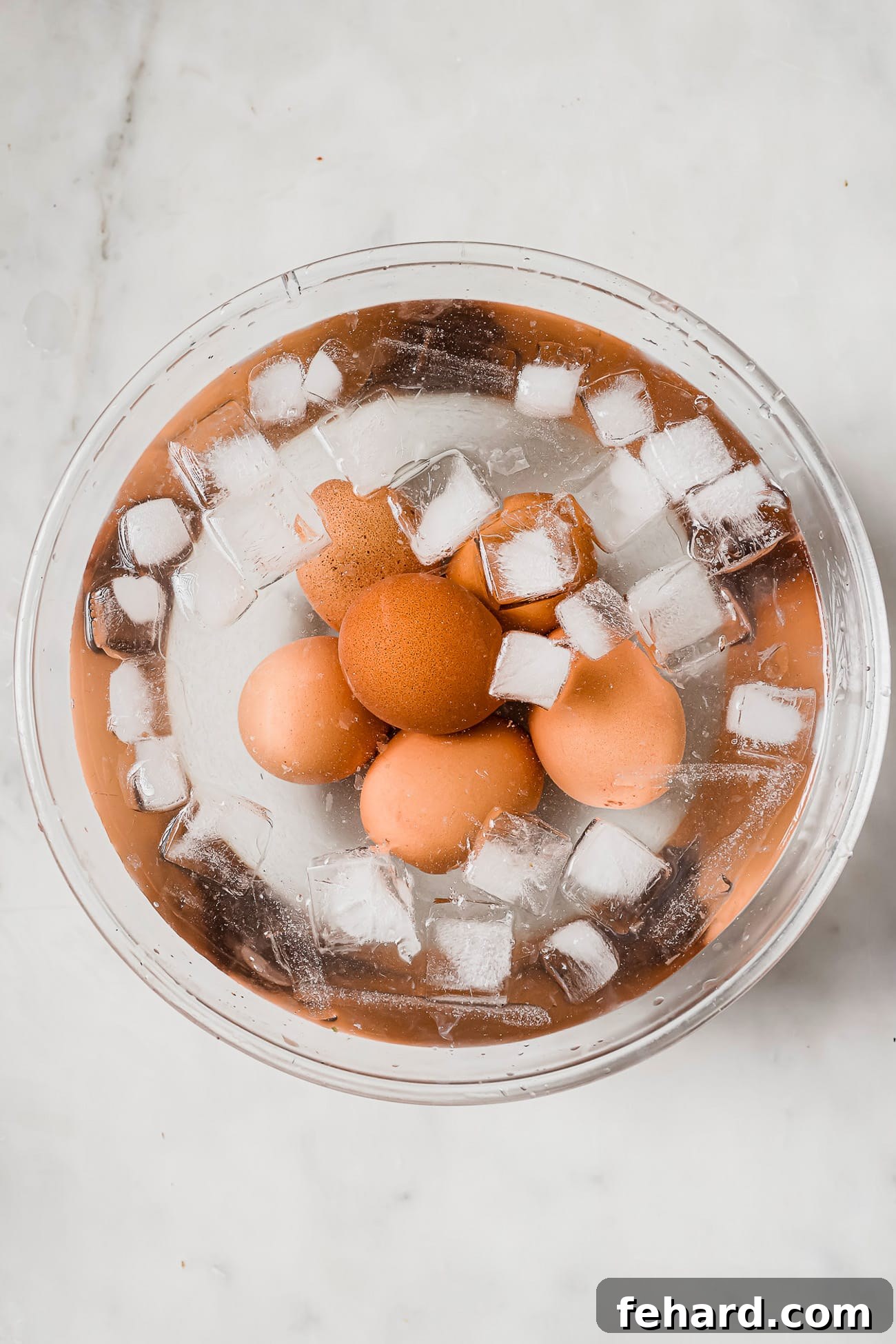Hard-boiled eggs submerged in a bowl of ice water, cooling down to prepare for peeling.