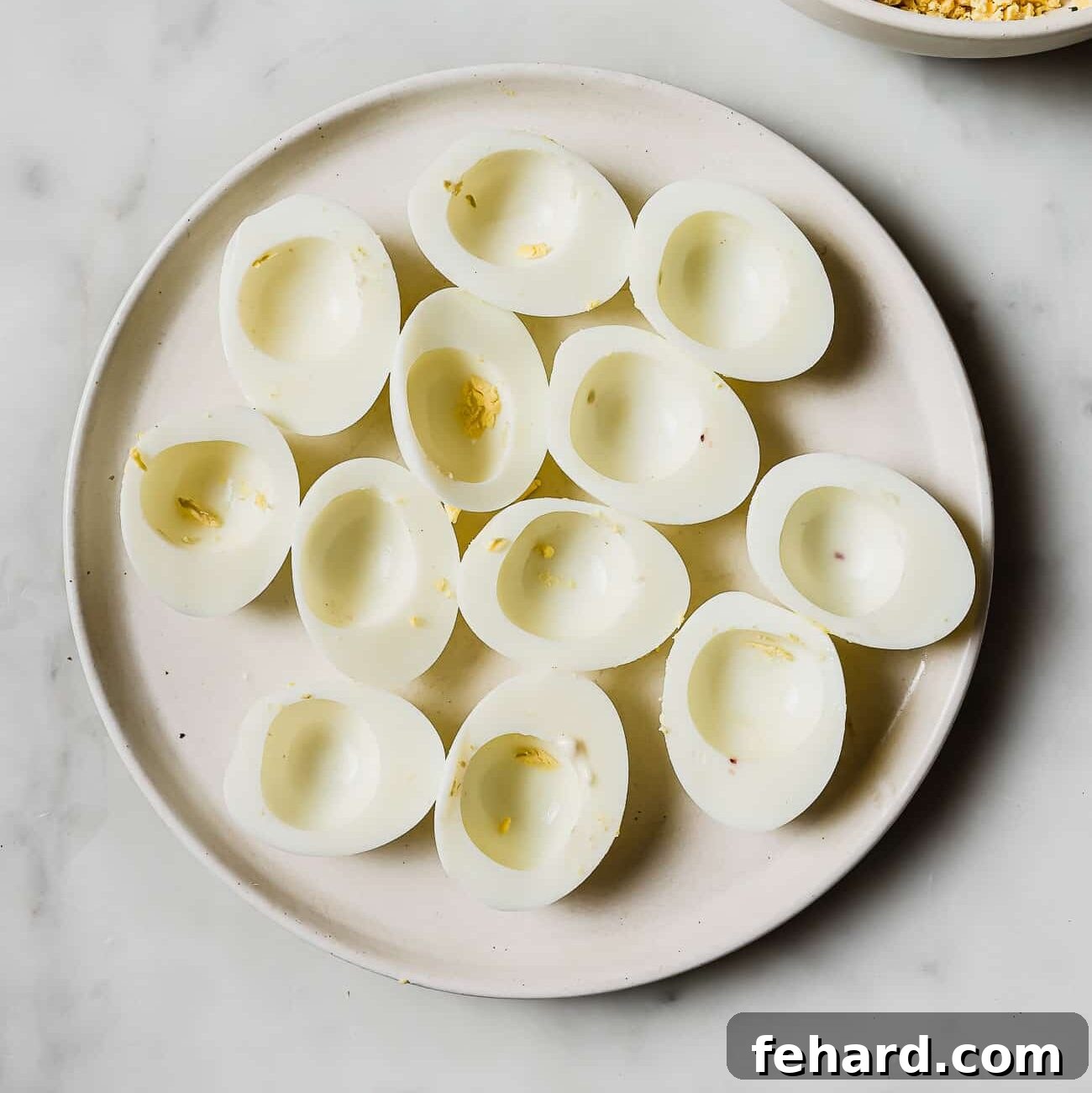 Halved egg whites perfectly arranged on a white plate, ready for the creamy yolk filling.